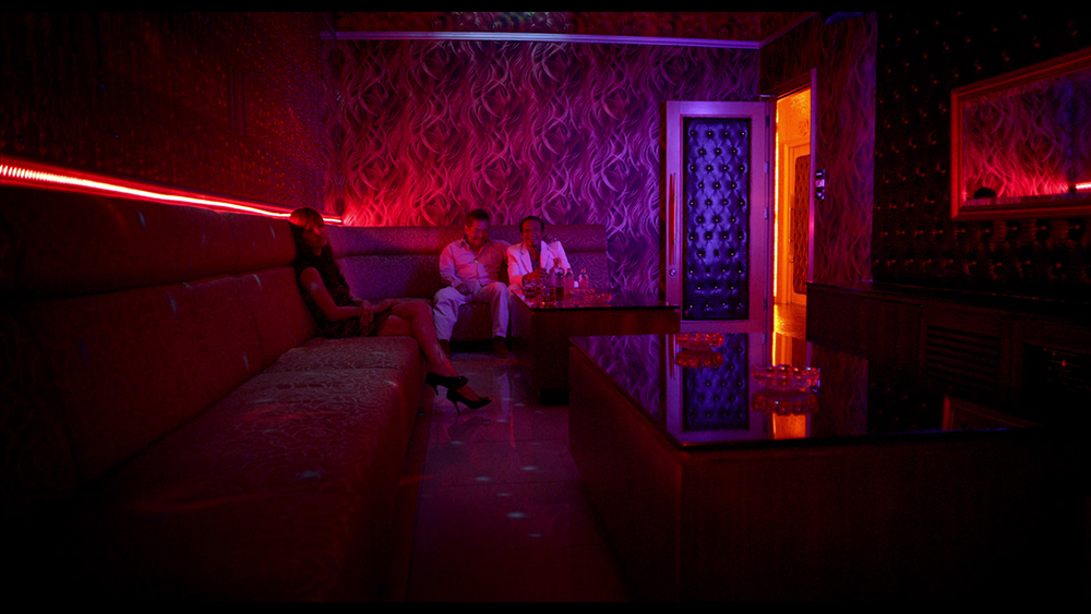 Una mujer y dos hombres en un cuarto iluminado con neón rojo. Películas con paisajes arquitectónicos.