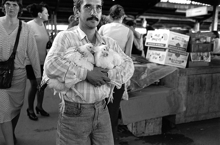 Hombre abrazando dos gallinas. Peter Kayafas. 